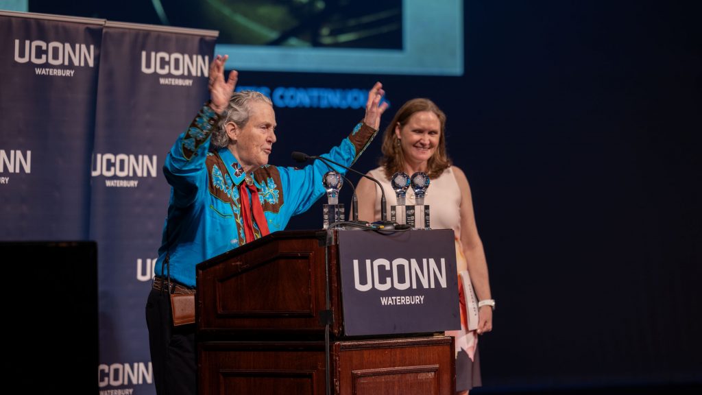 A woman in a Western-style shirt stands at a podium, addressing a crowd.