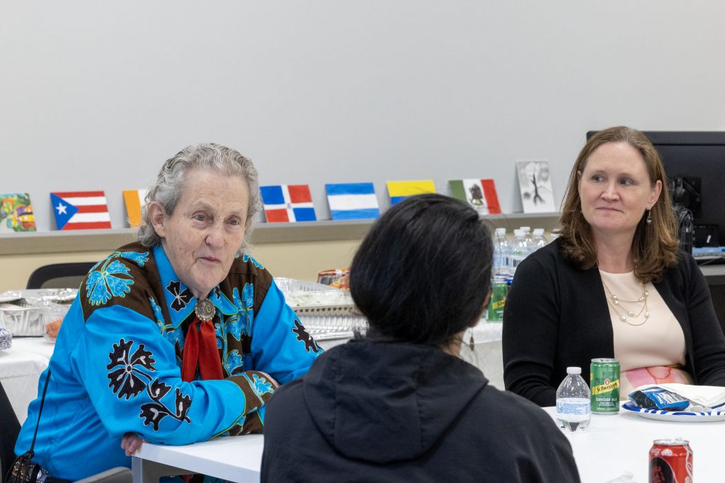 Three women sit at a table, speaking. 