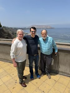 Three men stand in front of the ocean