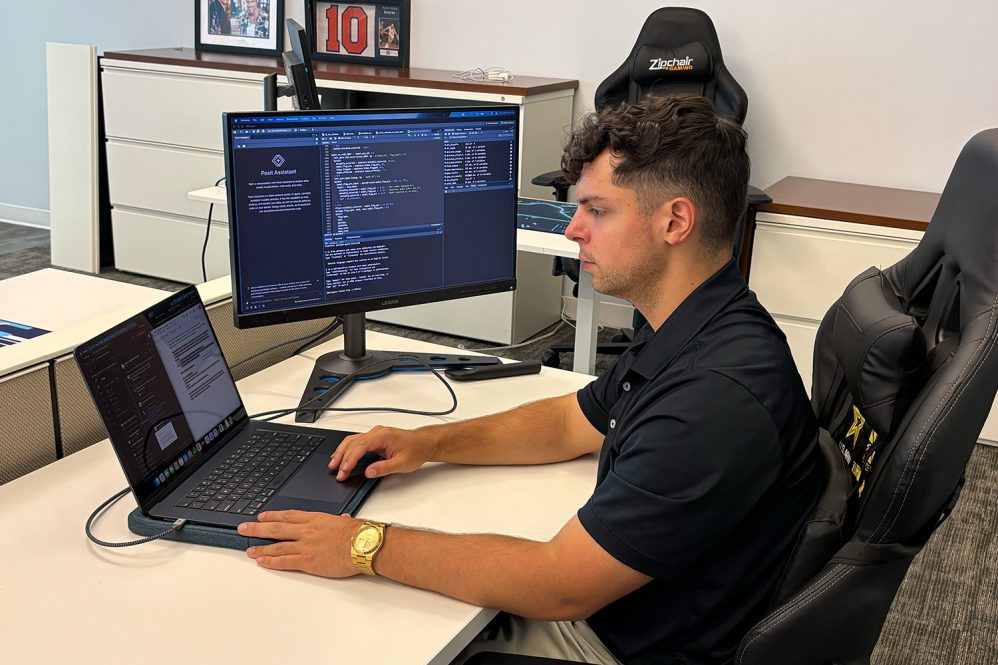 Student sits at desks in front of a laptop and desktop computer.