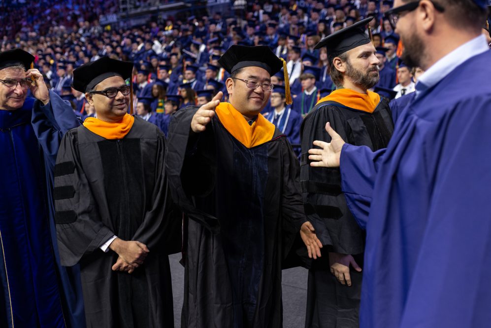 Two men about to shake hands at a commencement ceremony.