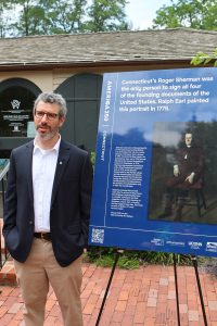 A man with a beard and glasses stands next to a poster board on an easel.