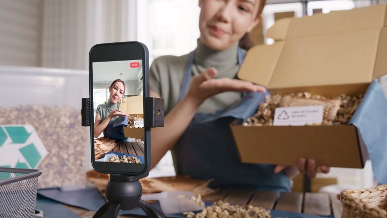 An influencer presents a boxed product to her cell phone camera.