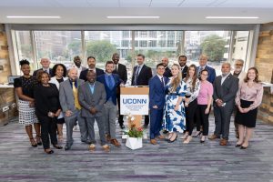 A group of people pose for a photograph in front of a podium with UConn branding.
