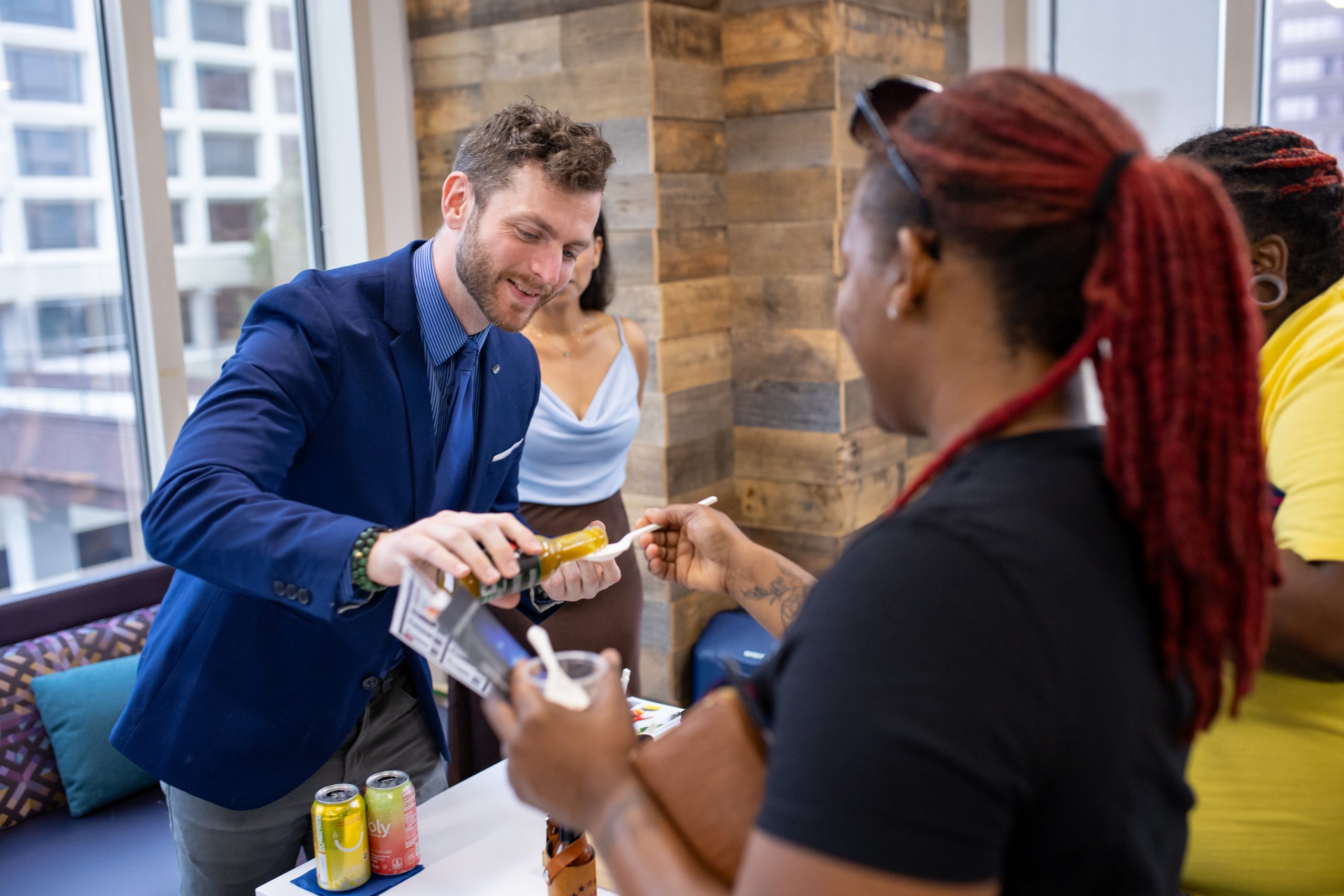 A man puts a sample of hot sauce on a piece of food being held out by a woman.
