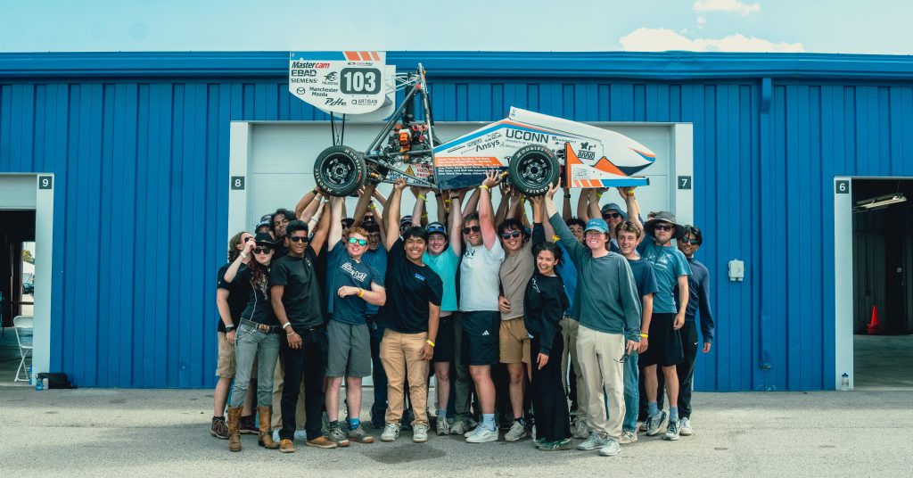 A large group of students holding up a small racecar above their heads.