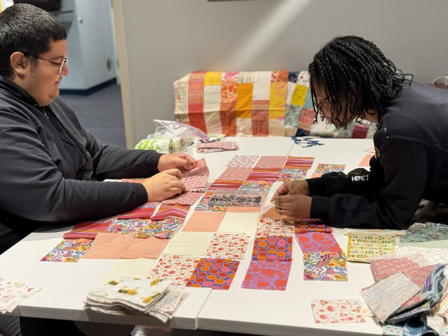 Two students working on a table sewing a quilt