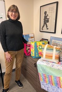 A woman in glasses and should-length hair stands next to bags on a table