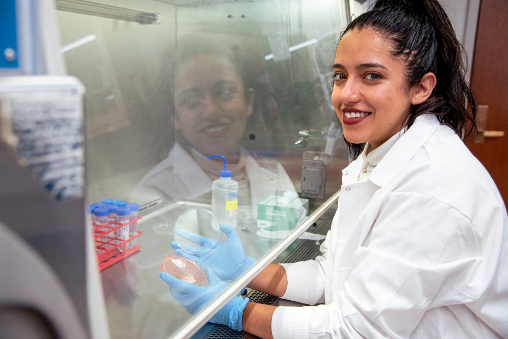 A woman in a white lab coat working in a lab, holding a dish