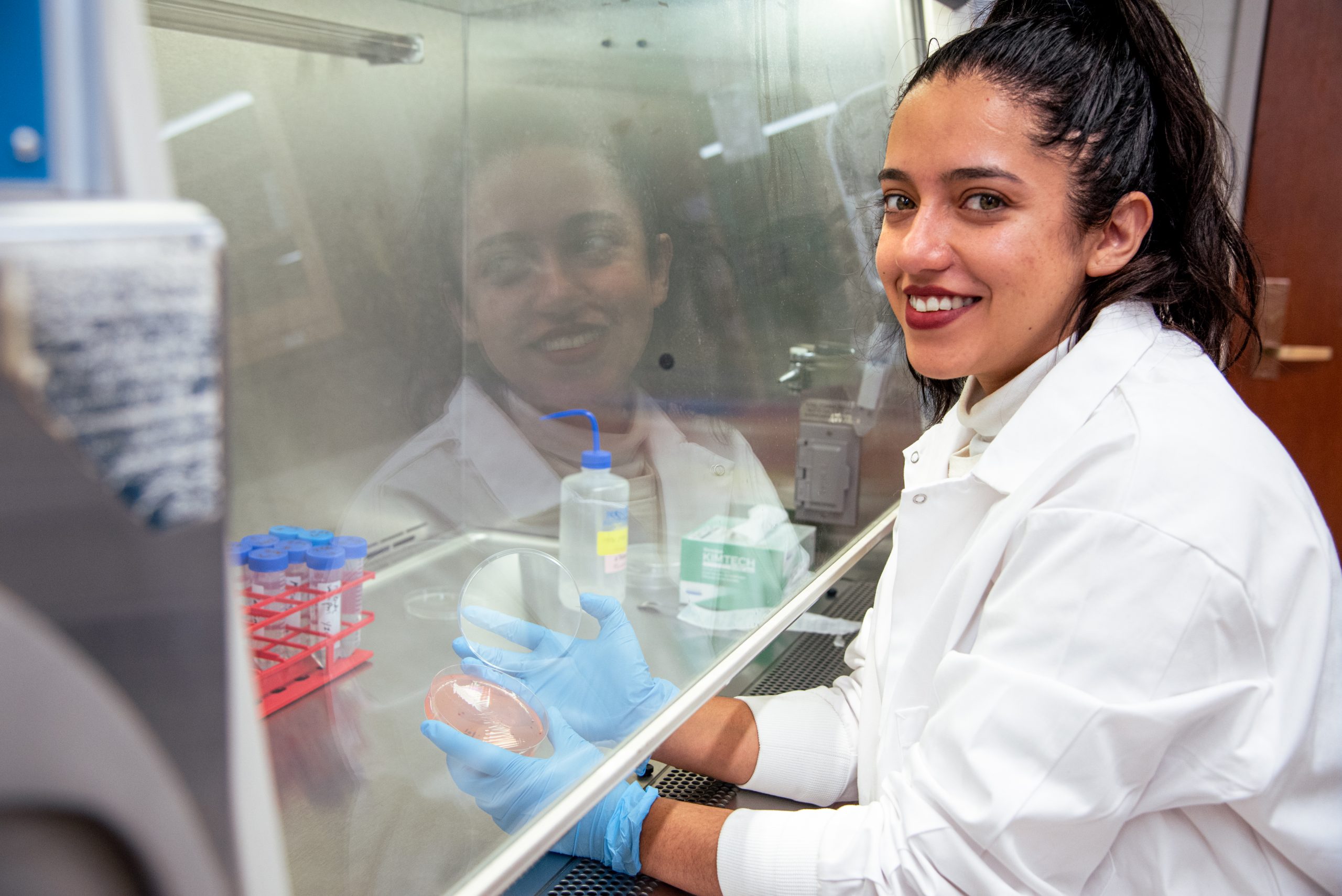 A woman in a white lab coat working in a lab, holding a dish