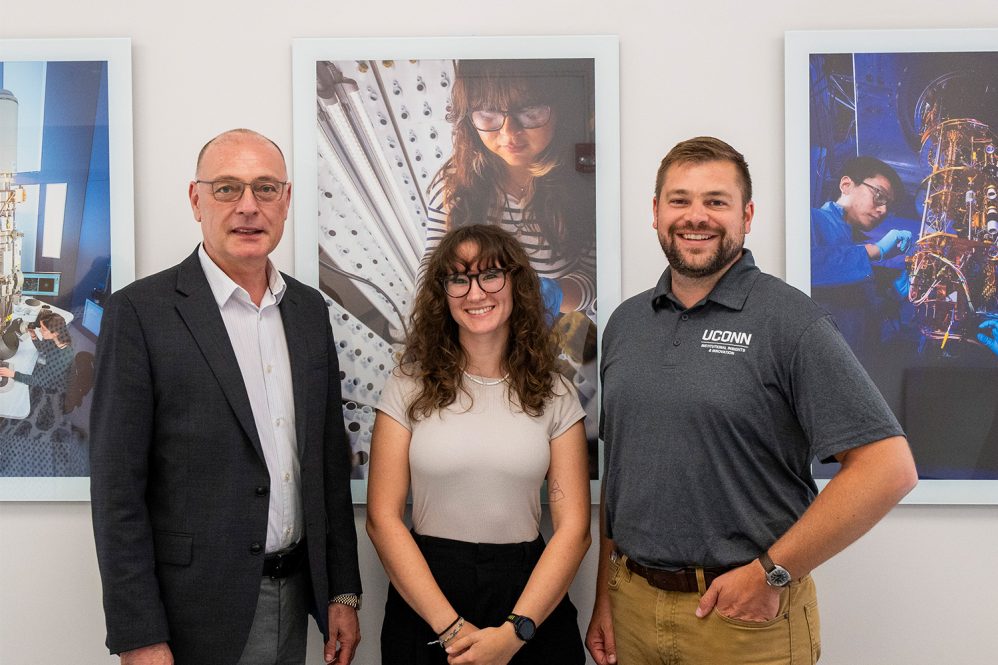 Two males and a female posing for a photo in front of posters