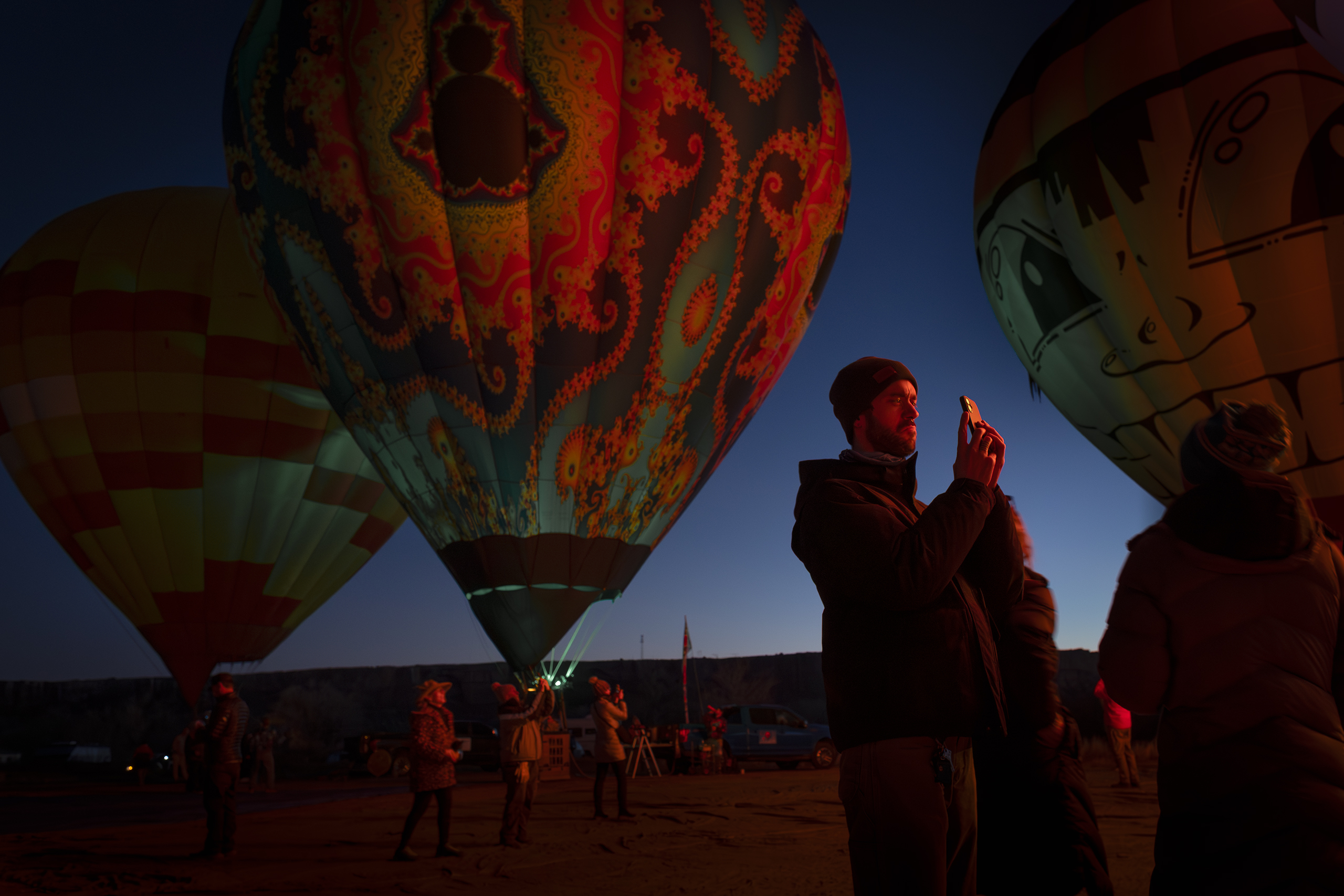 A person taking a photo of a hot air balloon at dusk