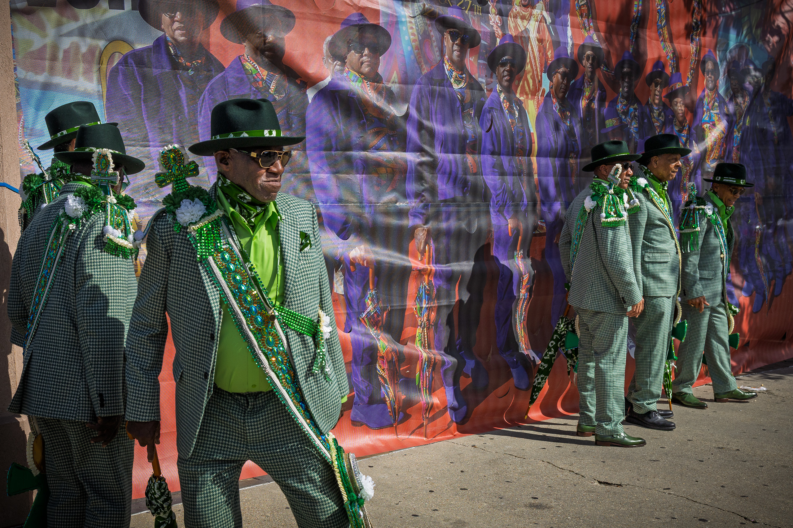 Six men dressed in green with hats posing for a photo next to a mural