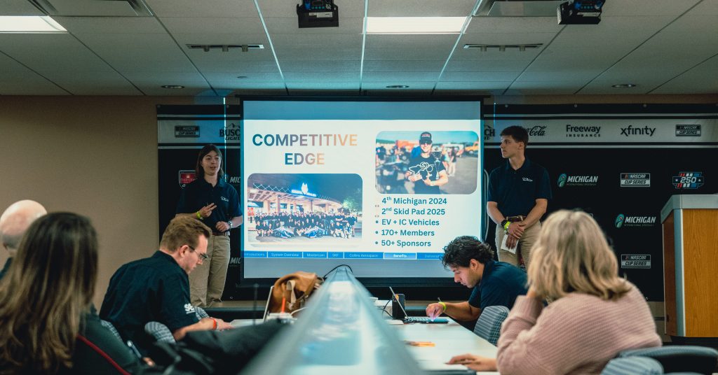 Two students making a presentation with several students looking on.