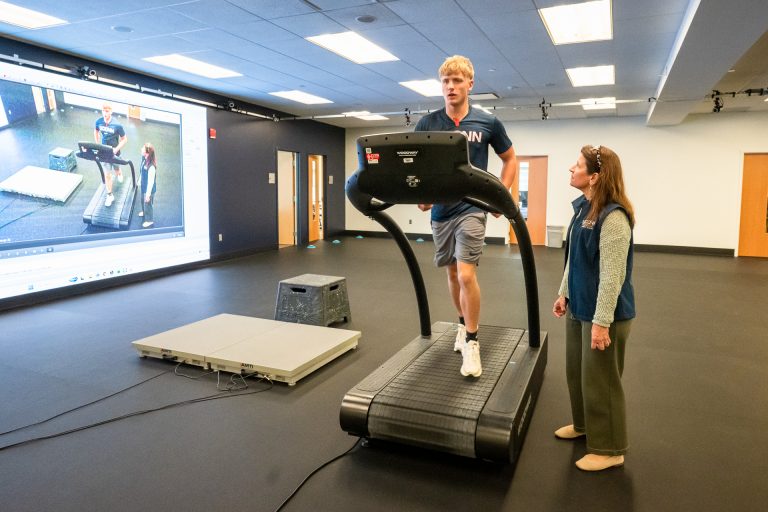 A man jogging on a treadmill while a woman watches
