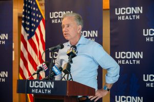 Governor Ned Lamont stands in a blue shirt at a UConn Health podium.