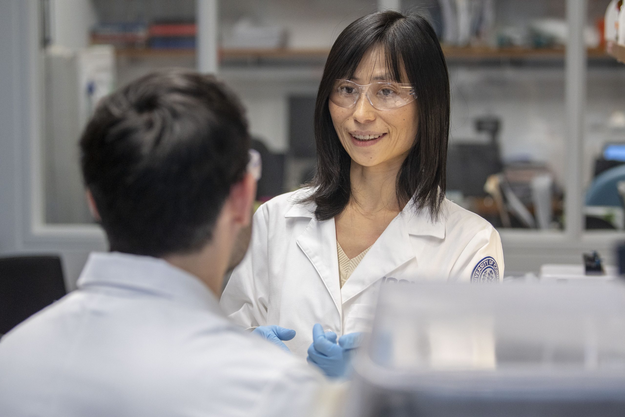 Woman with black hair in lab coat doing an experiment with a male student