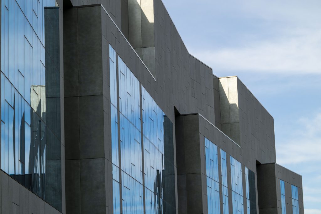 A portion of a grey building, with large windows reflecting the blue sky.