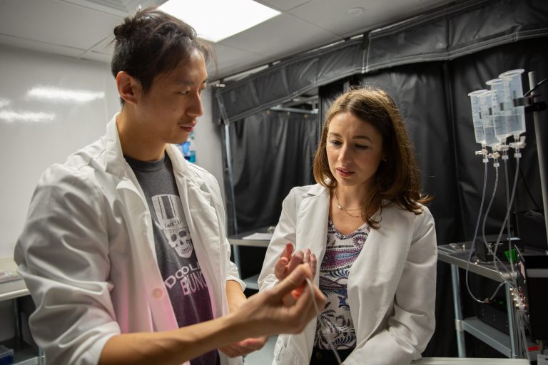 Two researchers examining a thin plastic tube in a laboratory