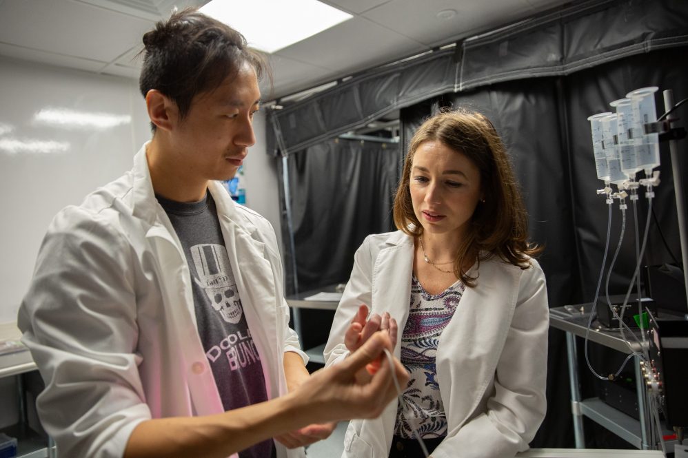 Two researchers examining a thin plastic tube in a laboratory
