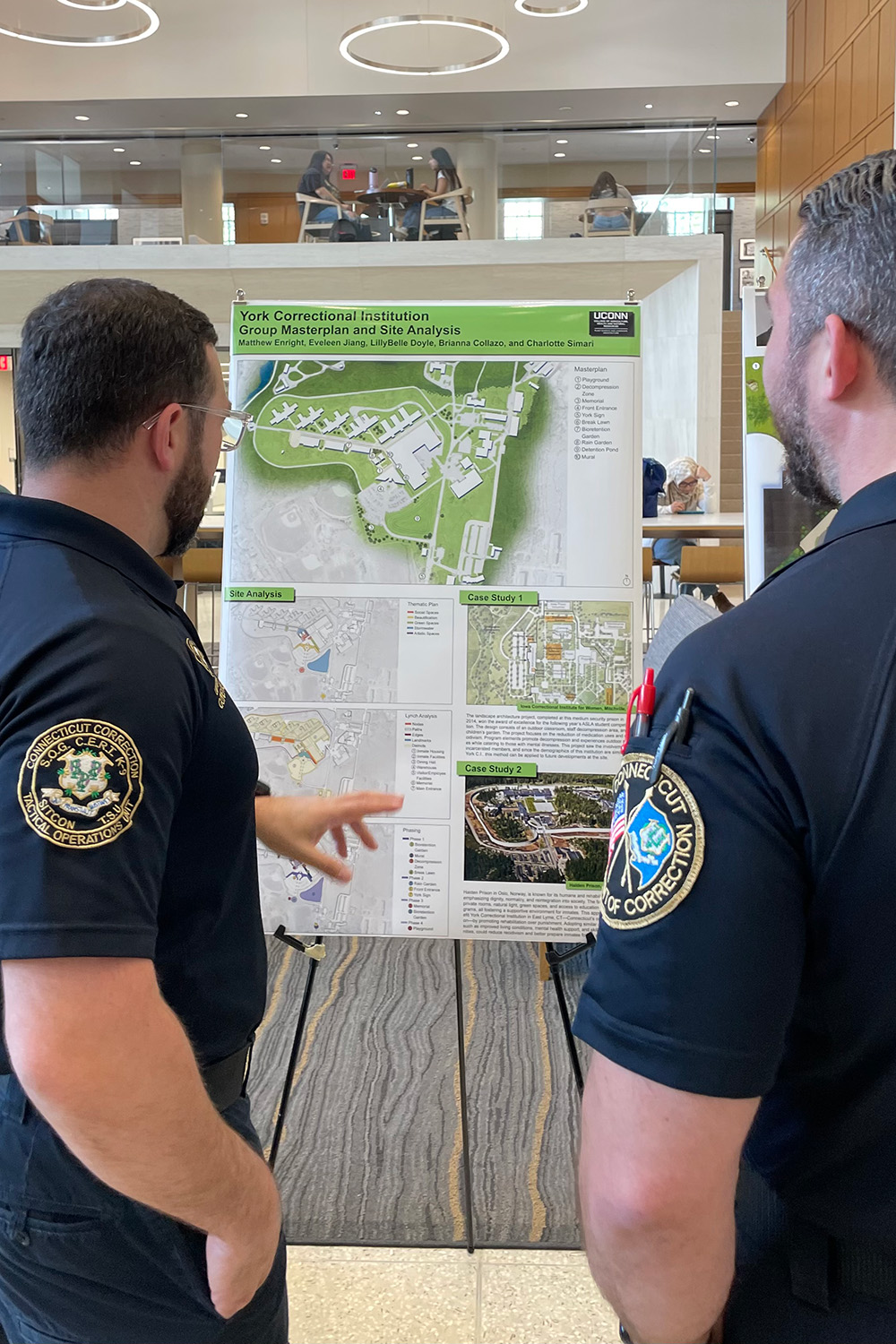 Two correctional officers look at a project poster in the atrium of the Hartford Times Building.