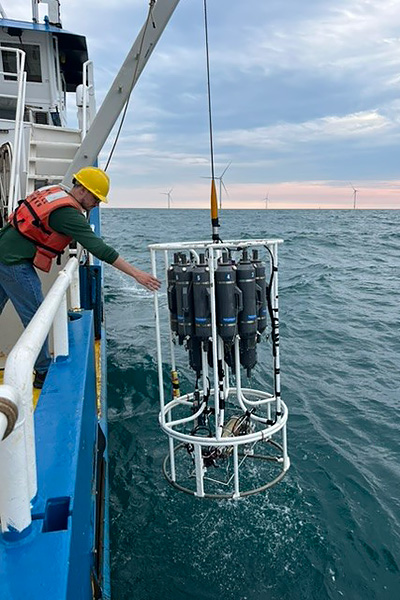 Students hold onto equipment hanging off the side of a research vessel on the ocean.