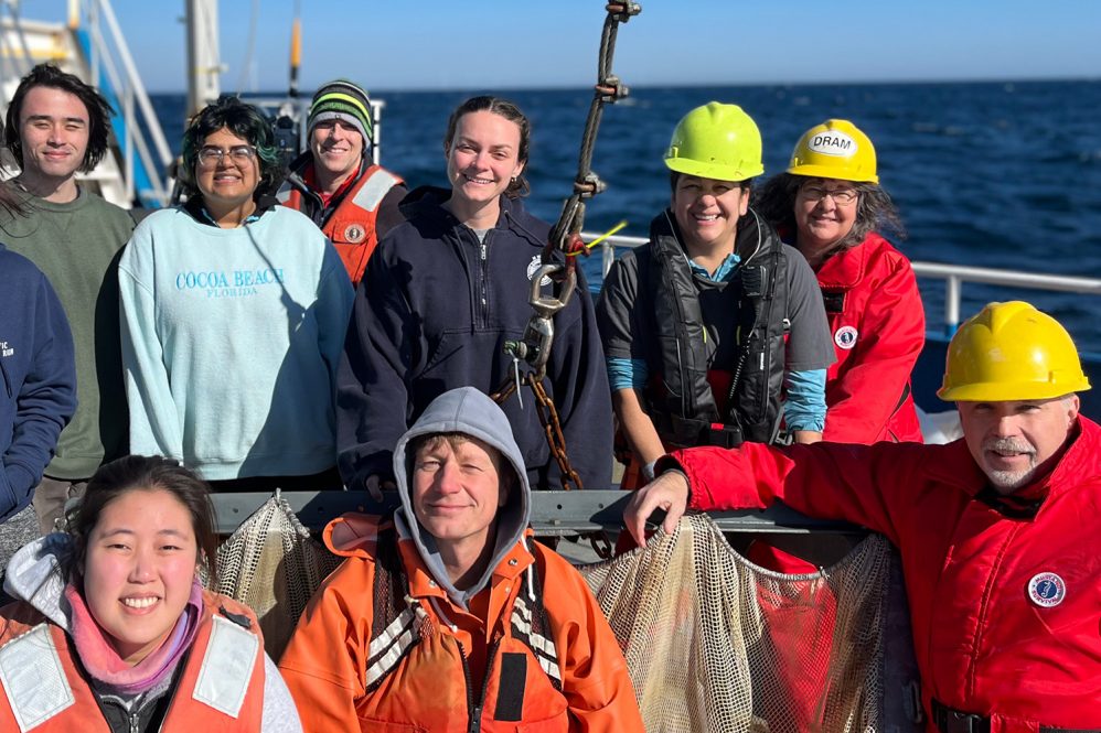 A group of marine scientists pose for a photo on the deck of a research vessel on the ocean.