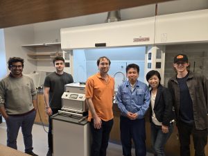 Six people stand together in a laboratory beside research equipment.