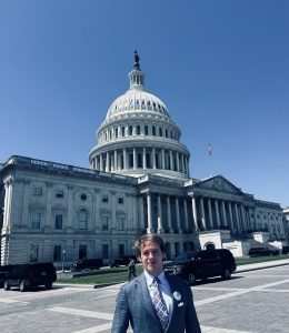 A person standing in front of the U.S. Capitol building on a sunny day with a blue sky in the background.