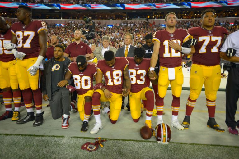 Members of a football team kneeling in yellow and burgundy uniforms