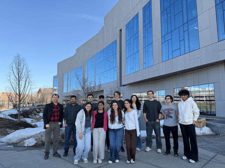 A group of students and researchers pose outside a modern campus building.