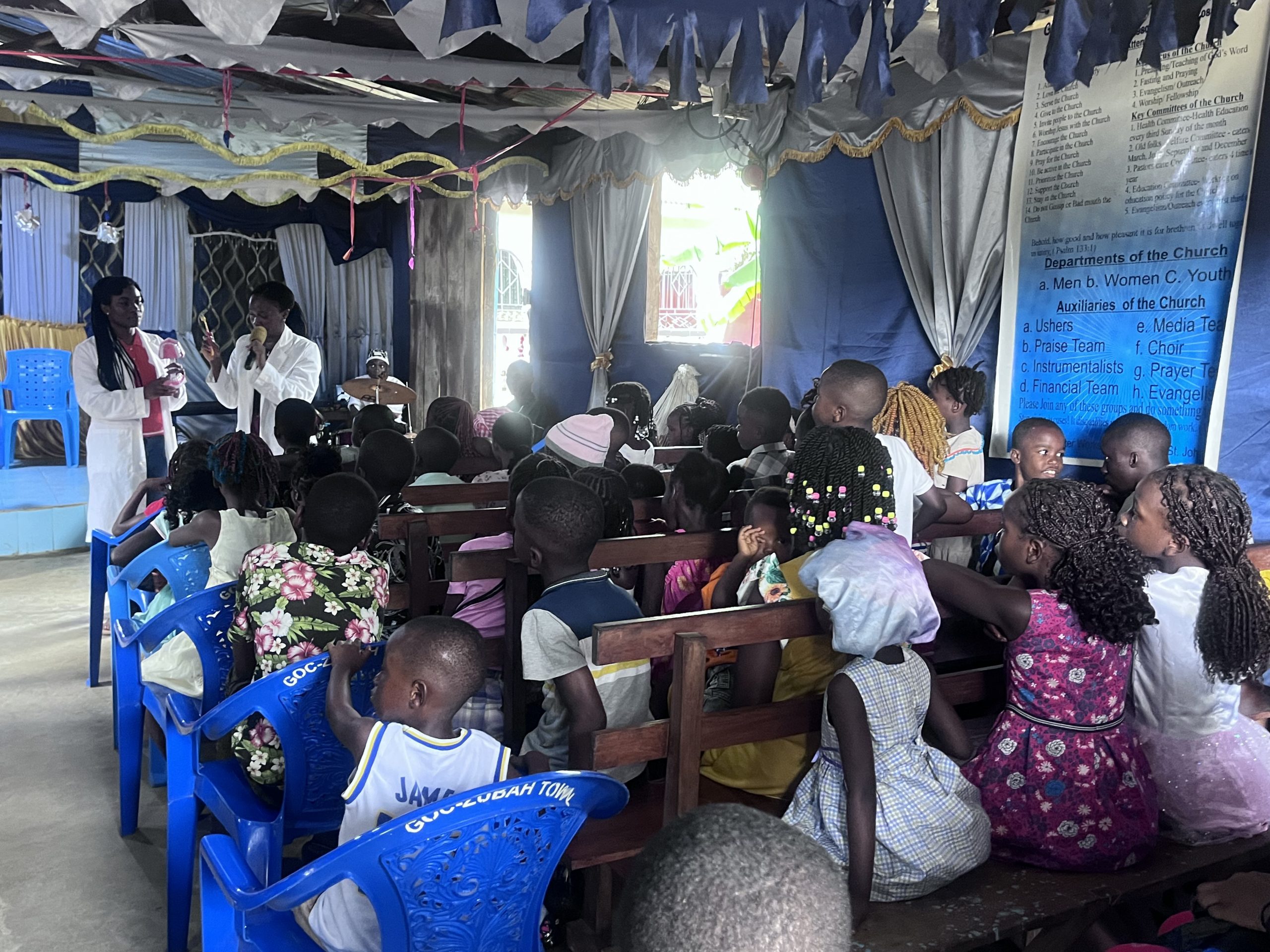 two women speaking to room of children
