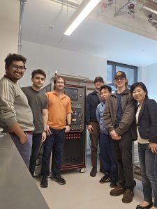 Seven people pose together beside specialized equipment in a research laboratory.