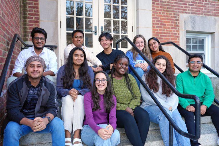 A group of researchers of various ages sits on the steps outside a UConn building