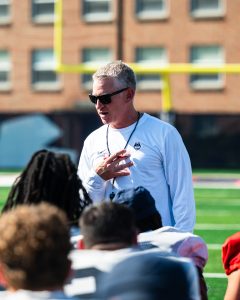 A man in sunglasses on a field talking to football players