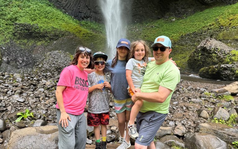 A man and a woman stand with their three children in front of a waterfall.