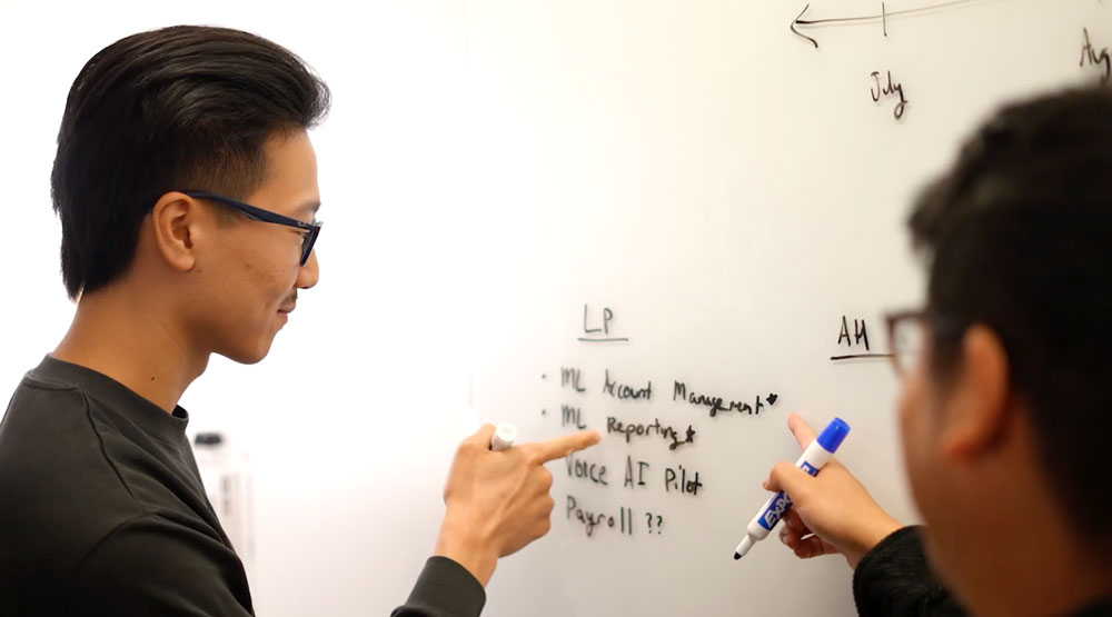 Two men are working on a white board