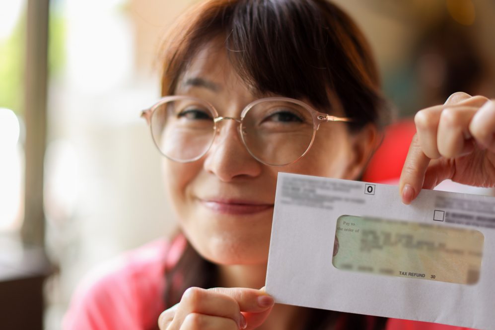 A woman holds up an envelope showing a tax refund.