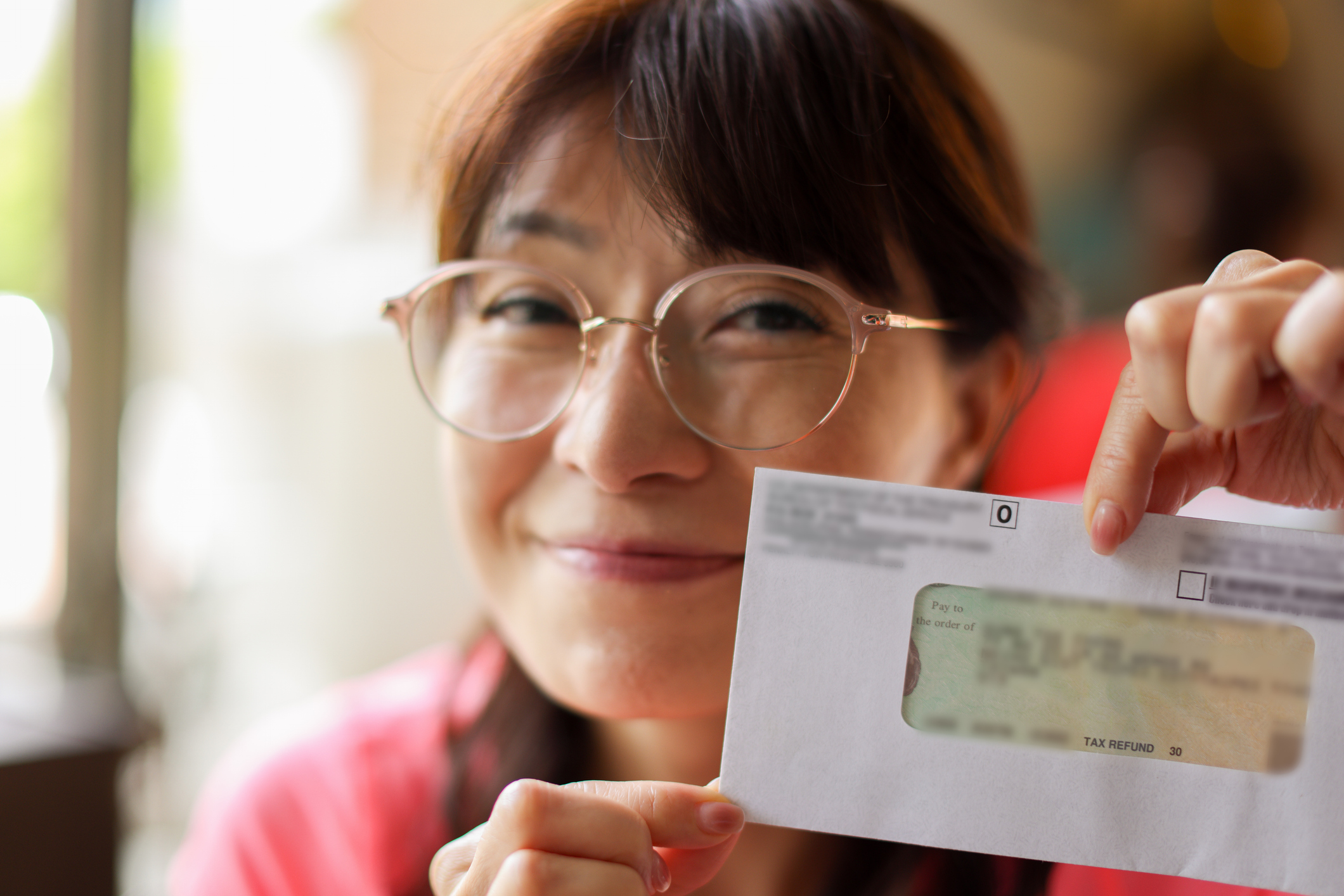 A woman holds up an envelope showing a tax refund.