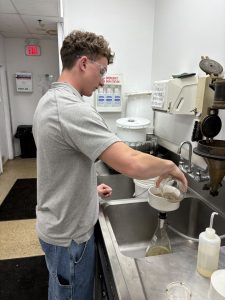 A student wearing safety glasses pours material through laboratory filtration equipment.