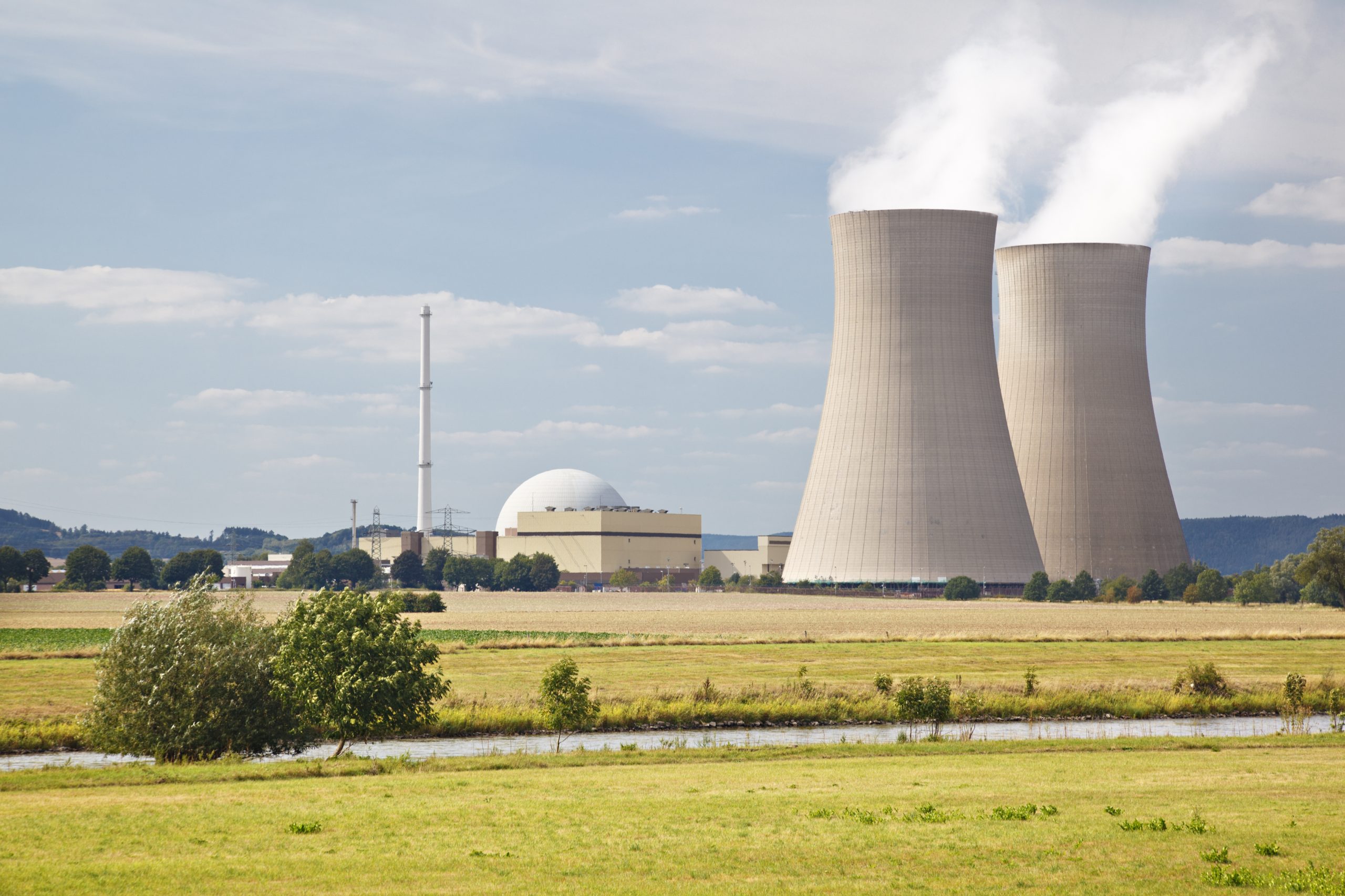 A nuclear power station with two large cooling towers releasing steam across a rural landscape.