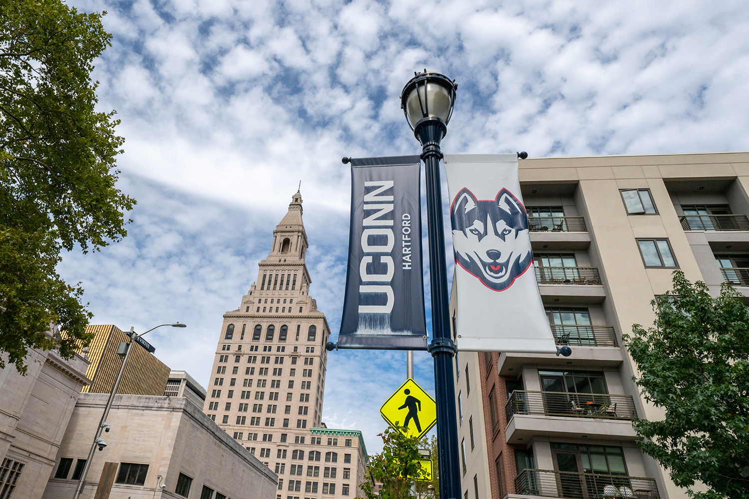 A UConn Hartford light poll banner in front of the Hartford skyline.