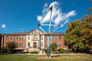UConn campus building behind a large geometric metal sculpture on a sunny fall day.