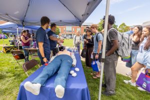 A CPR dummy lies on a table while students await a demonstration.