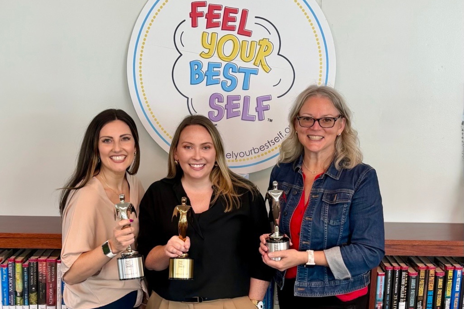 Molly Ferreira, Emily Wicks, and Sandra Chafouleas pose for a photo, each holding a Telly Award, shaped like a metal statue.
