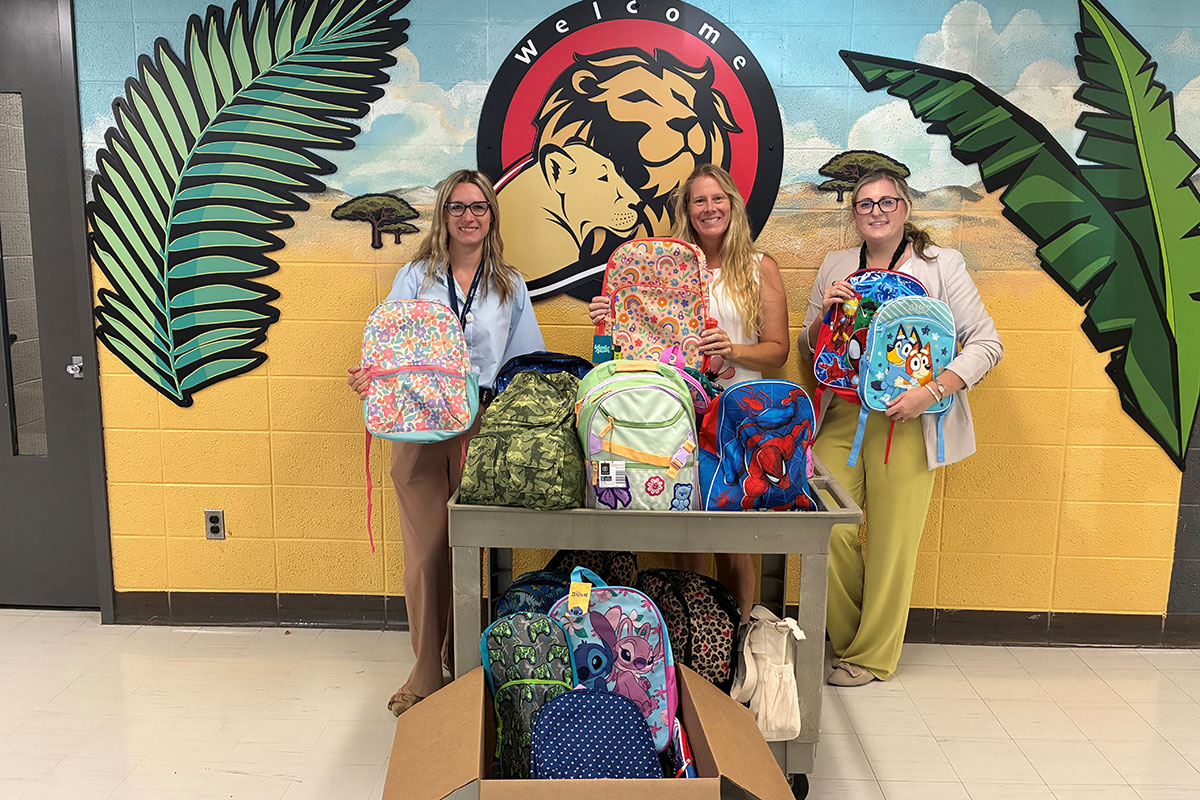 portrait three women showing donated backpacks of school supplies