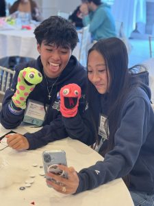 Two adolescent students play with colorful hand puppets.