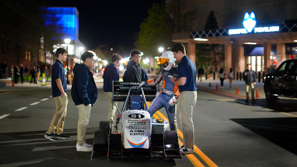 UConn Formula SAE team members gather around a race car on a campus street at night