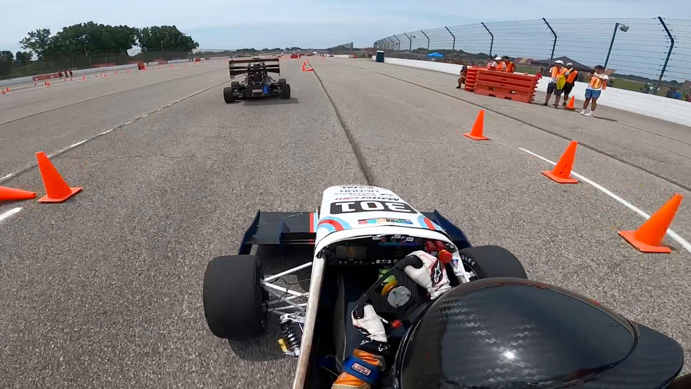 Driver in a UConn Formula SAE race car navigates a cone-marked test track