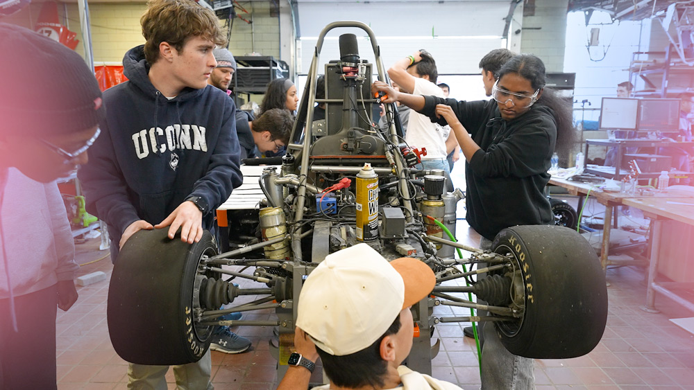 UConn students work together on a Formula SAE race car in an engineering workshop.